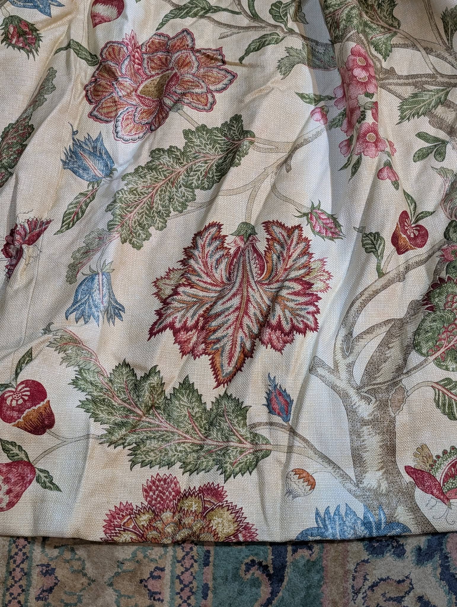 Close-up of beige fabric with large pink, red, and blue flowers and green leaves pattern.