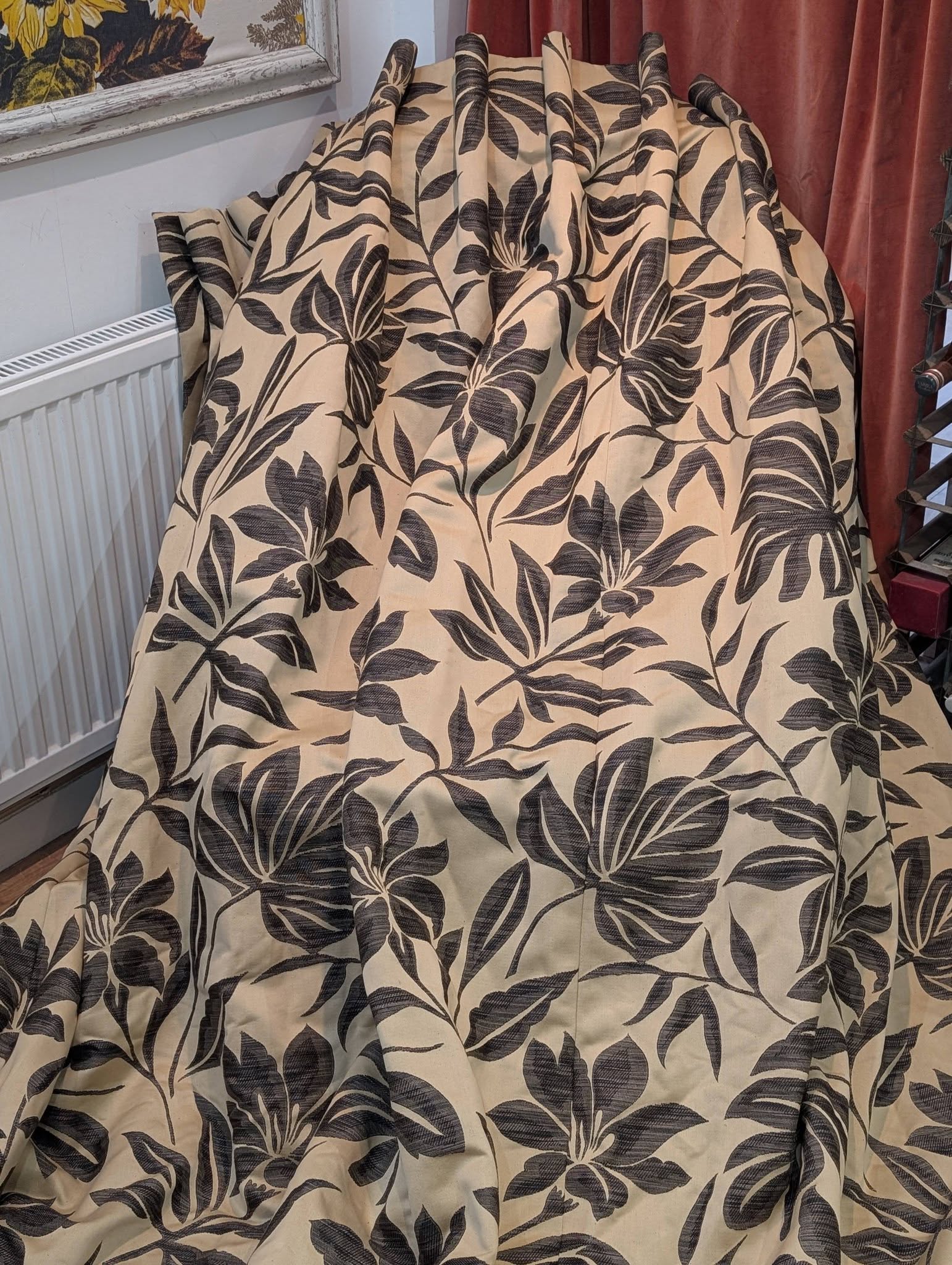 Beige fabric with a large dark botanical leaf pattern draped over a chair or surface, creating a decorative textile look.