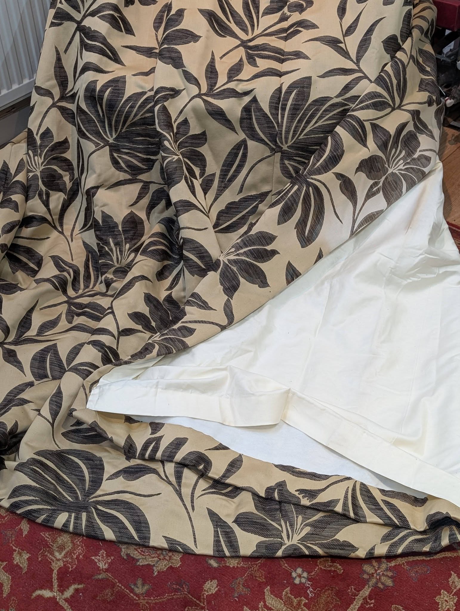 Beige fabric with a dark botanical leaf pattern laid over a chair, resting on a red floral carpet.