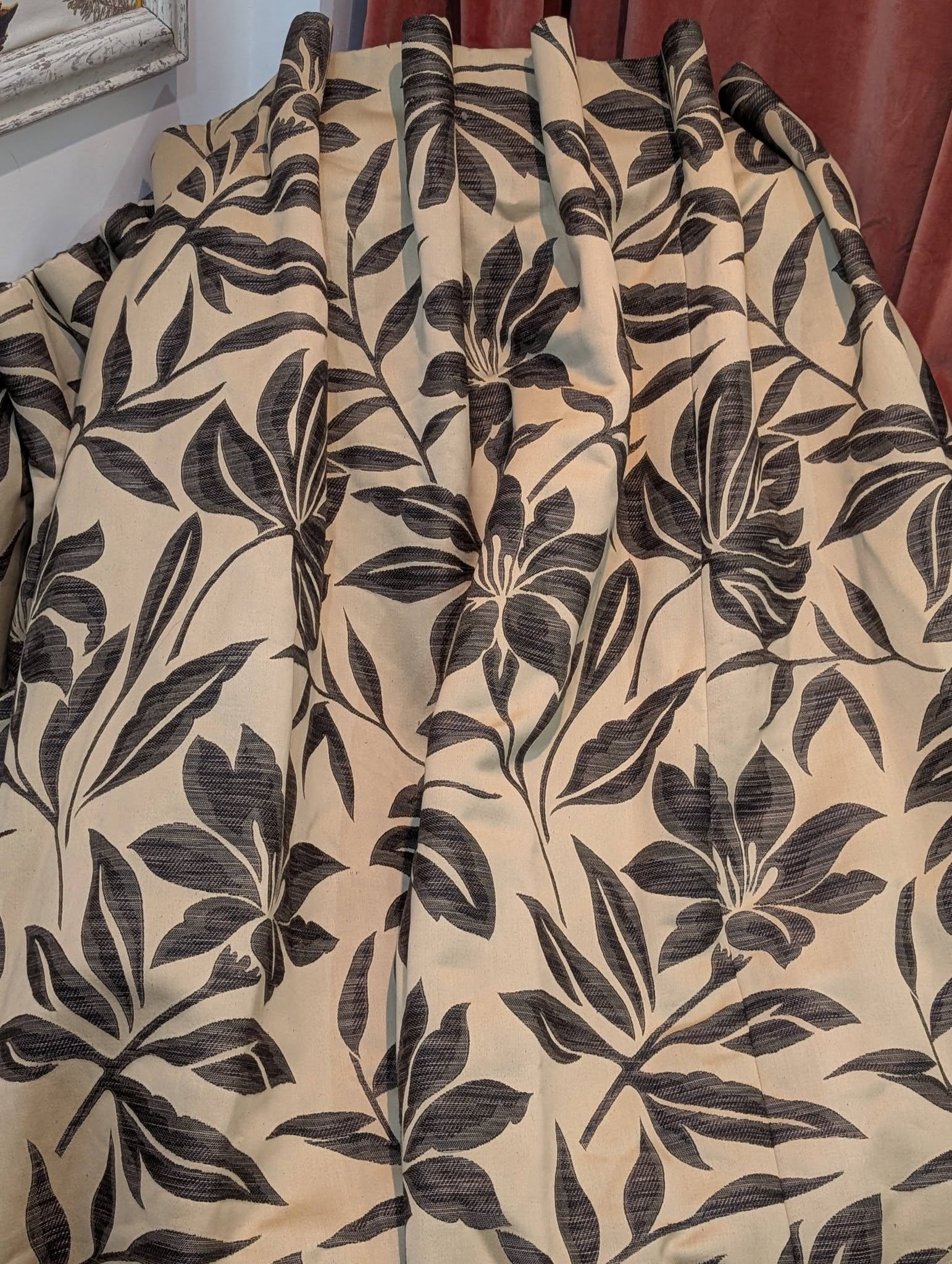 Beige fabric with a bold black botanical leaf pattern, shown draped in soft folds (fabric texture visible).