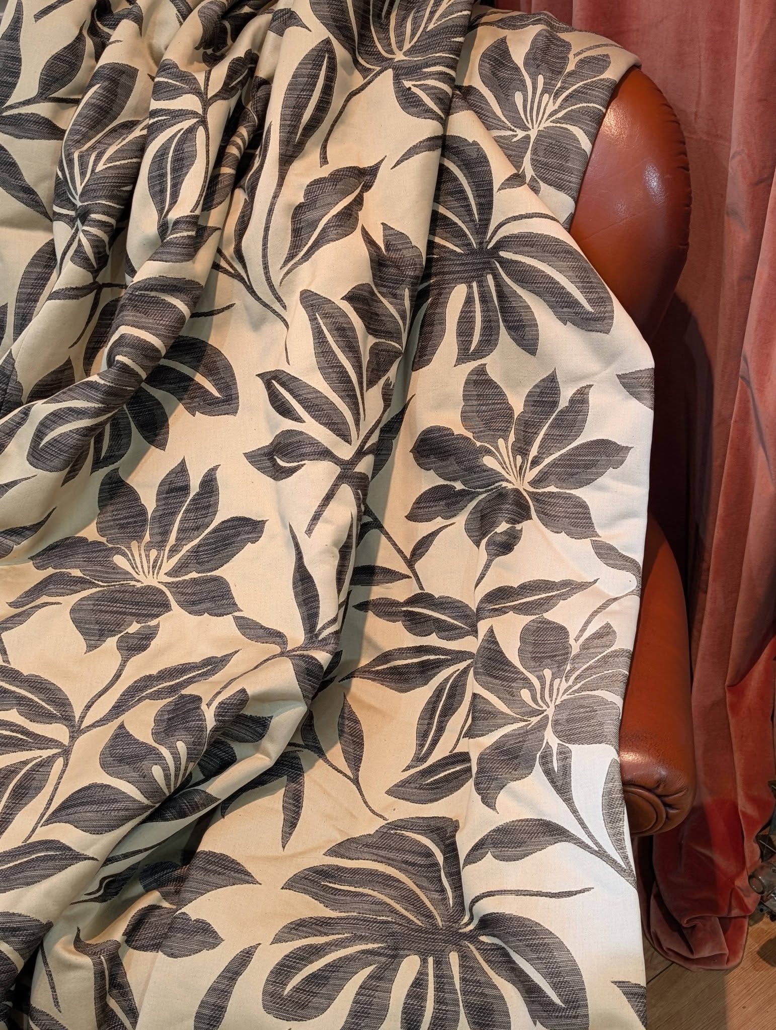 Beige fabric with a dark blue-gray botanical leaf pattern draped over a brown leather chair.