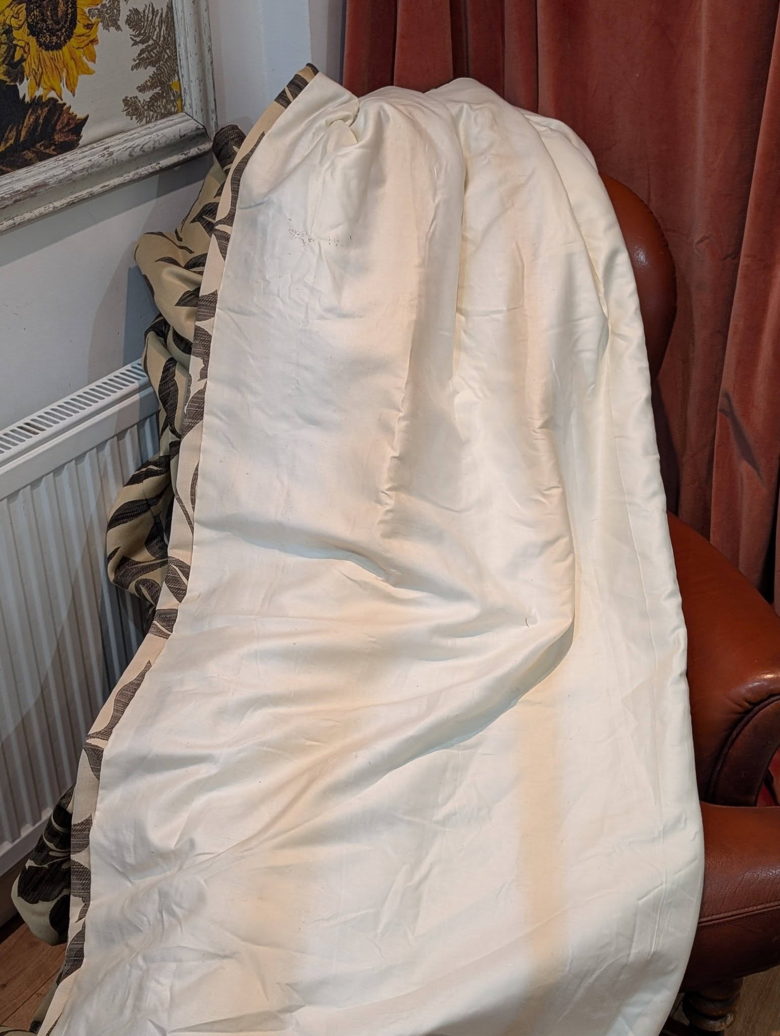 Chair draped with a white sheet in a living room corner, beside a radiator and red curtains.